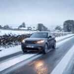 Modern high-class luxury SUV driving through a heavy snowstorm on a narrow British country road